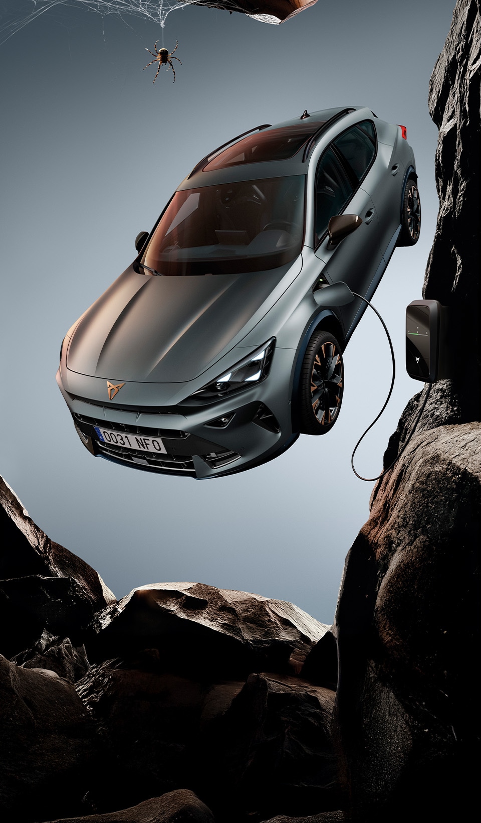 A CUPRA Formentor CUV suspended diagonally, next to a rocky, cliff-like structure. A charging cable is connected to the car from a charging unit on the cliff face.