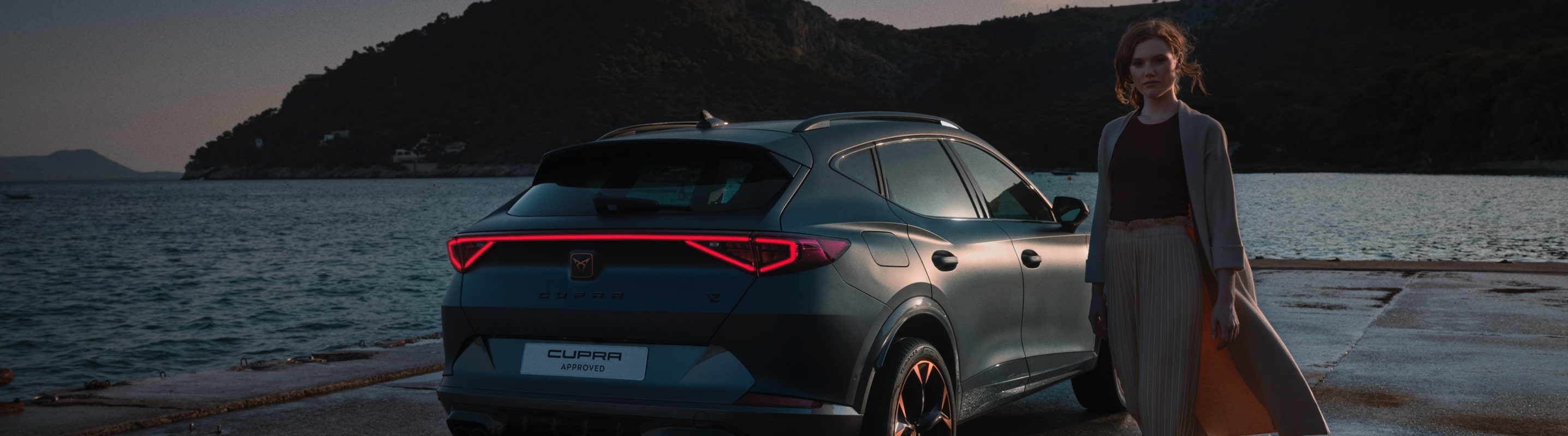 a woman standing next to a rear view of a cupra ateca rodium grey car with full led headlights