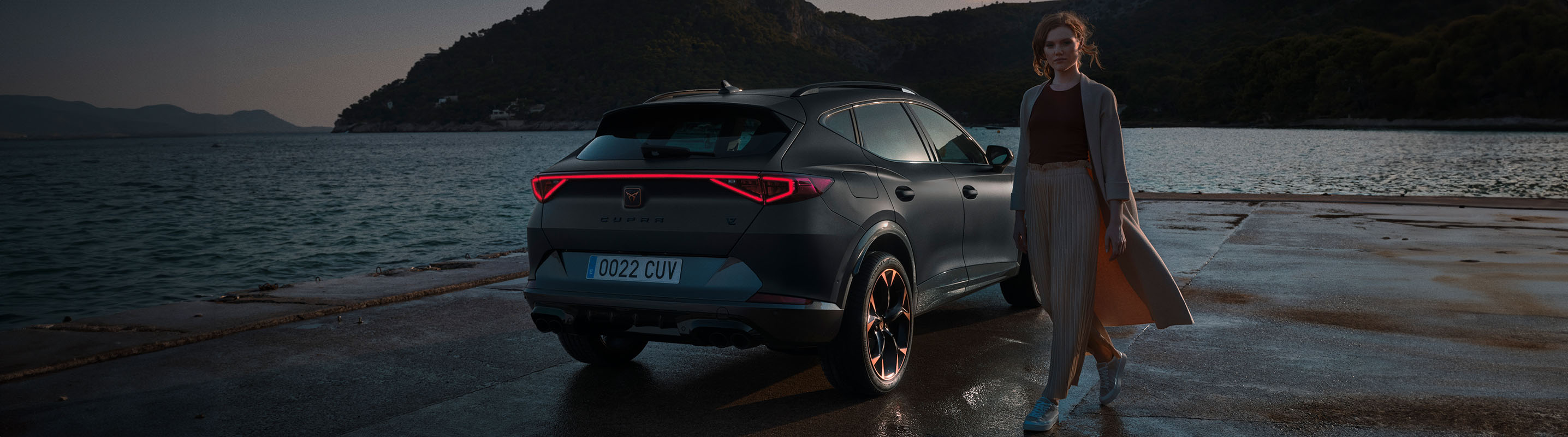 a woman standing next to a rear view of a cupra ateca rodium grey car with full led headlights