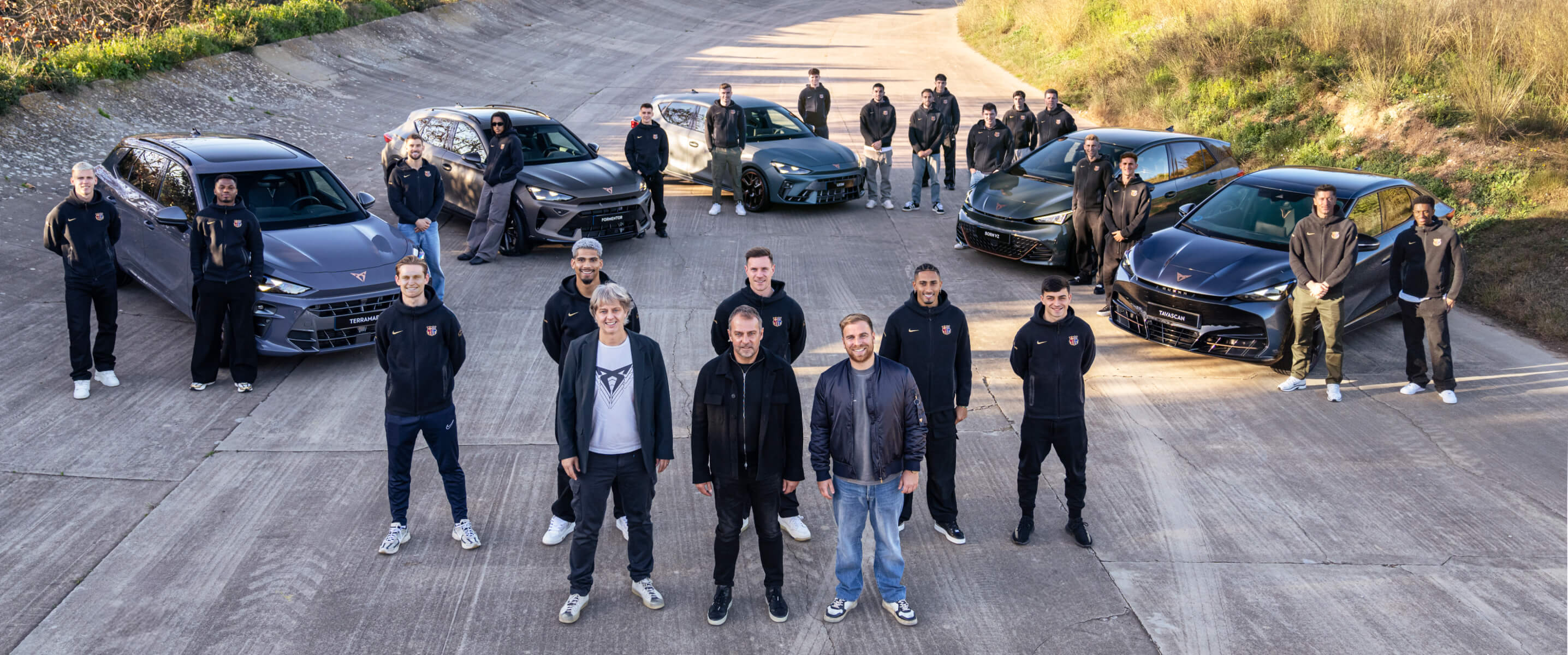 A football team and automotive brand representatives, pose together in front of several CUPRA vehicles on a sloped track surrounded by nature.