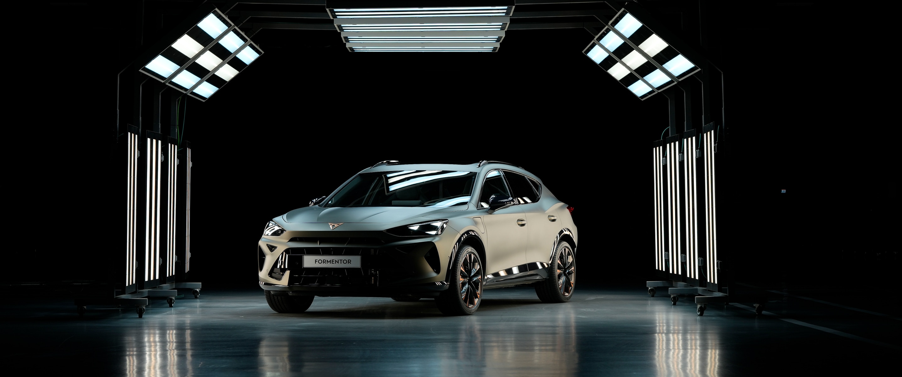 A CUPRA Formentor is centered in a completely dark studio, brilliantly illuminated by an array of bright overhead and vertical panel lights, which reflect off the glossy floor.