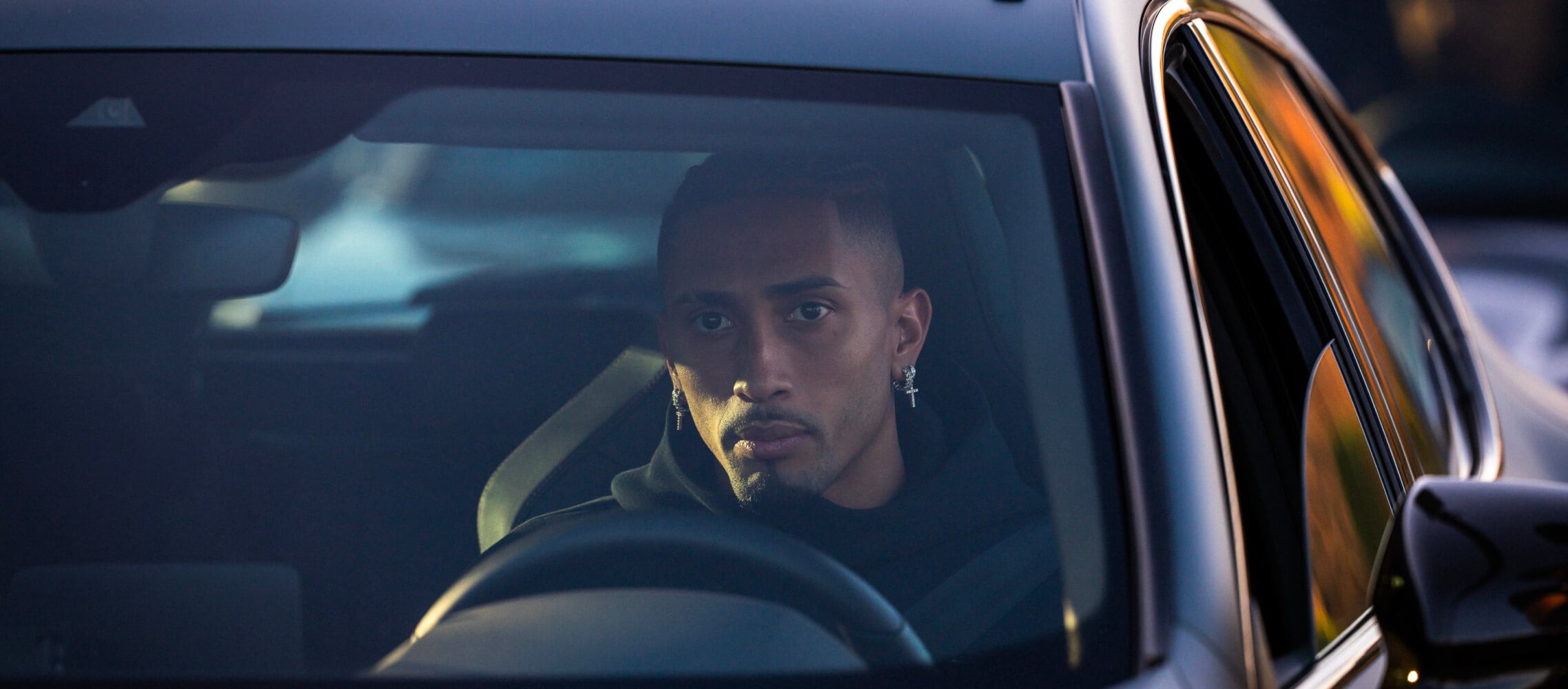 Raphinha, FC Barcelona player, sits in the driver’s seat of a car, looking straight ahead. 