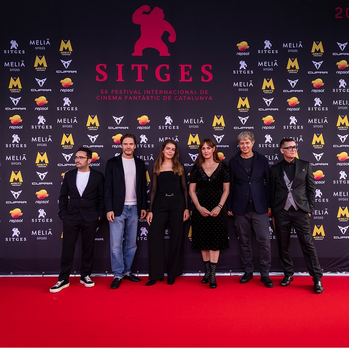 A group of six people, including actors and filmmakers, stand on the red carpet at the Sitges Film Festival 2025. A large Sitges logo is behind them, with a sponsor wall and a skull graphic on the right.