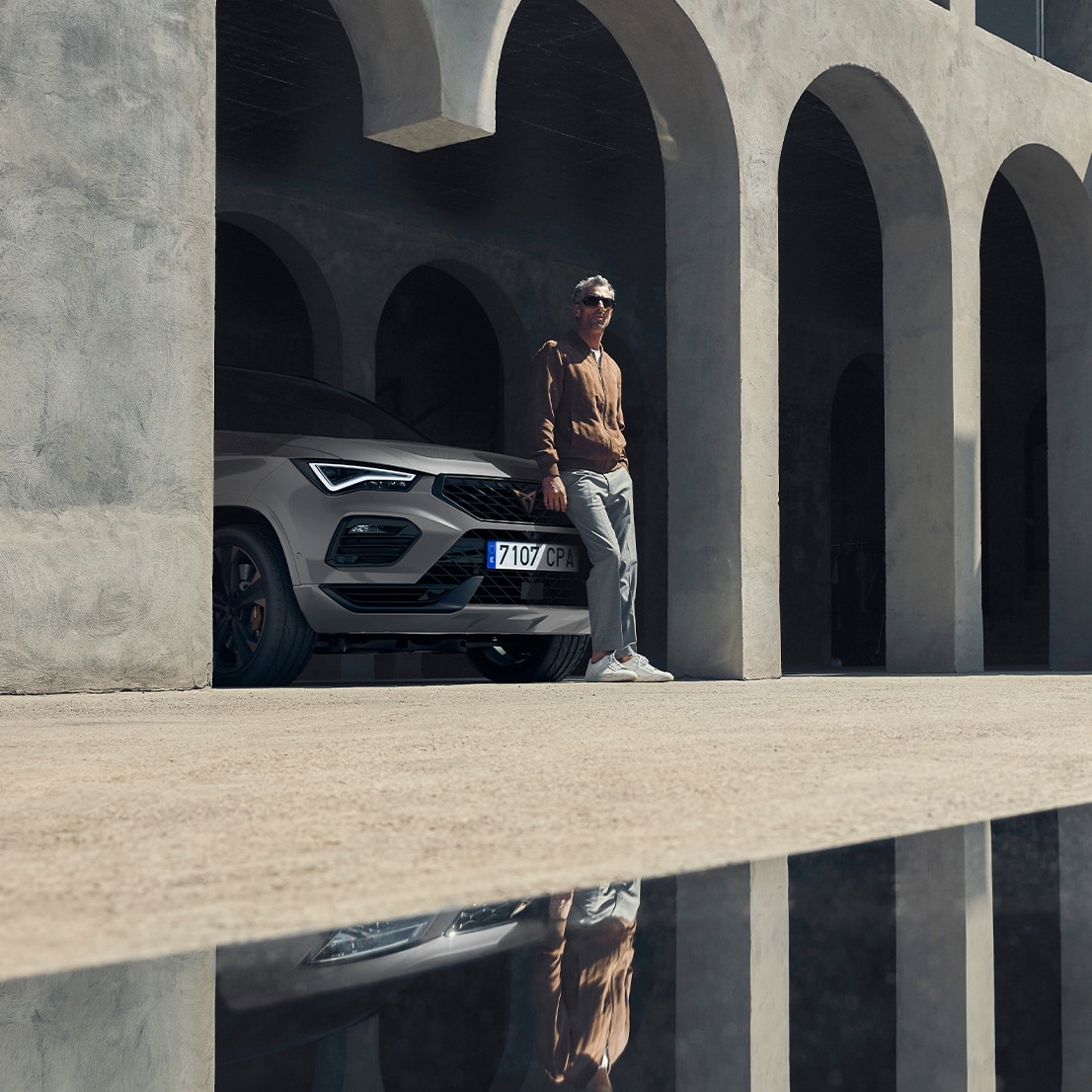 A man leaning on a parked metallic-coloured CUPRA Ateca.