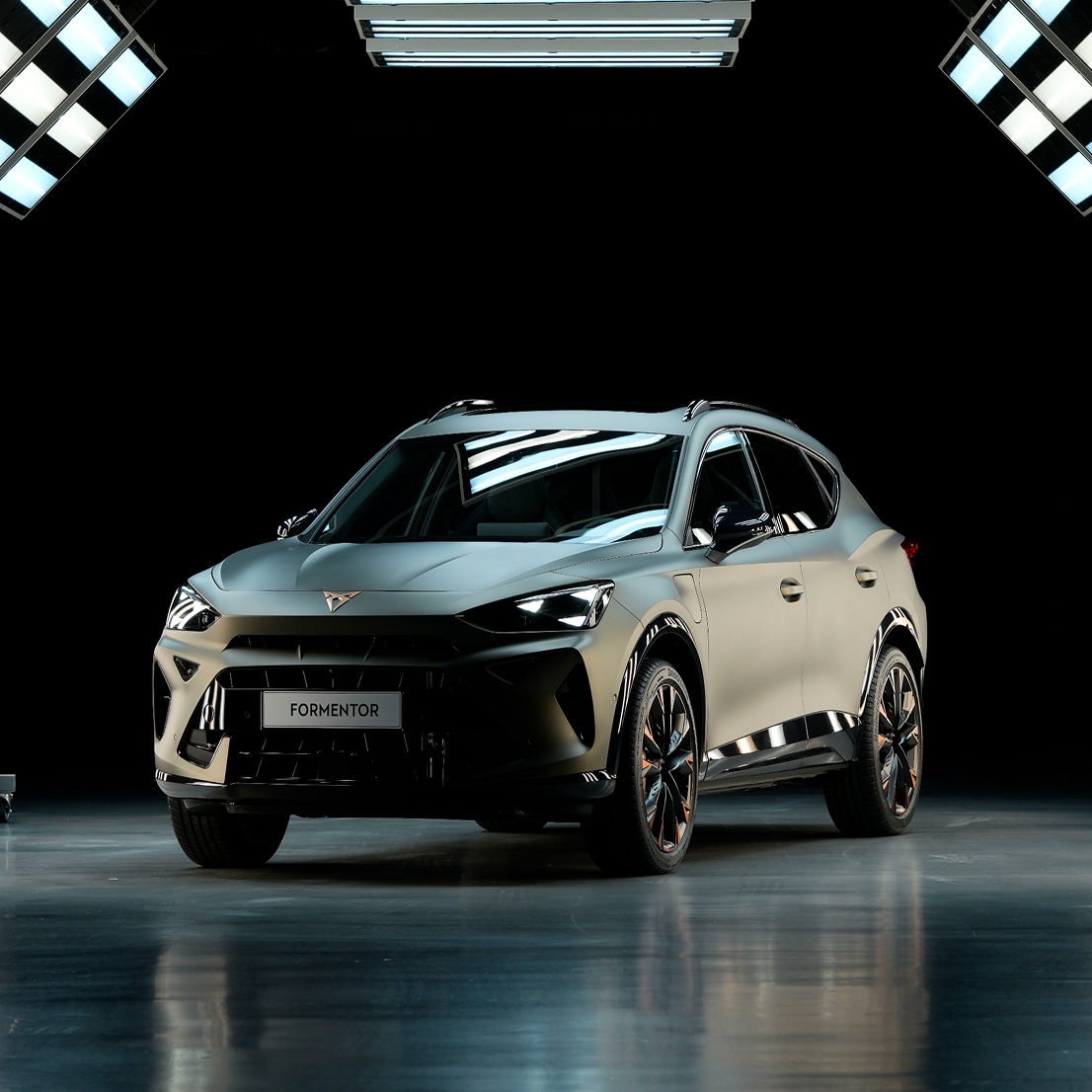 A CUPRA Formentor is centered in a completely dark studio, brilliantly illuminated by an array of bright overhead and vertical panel lights, which reflect off the glossy floor.