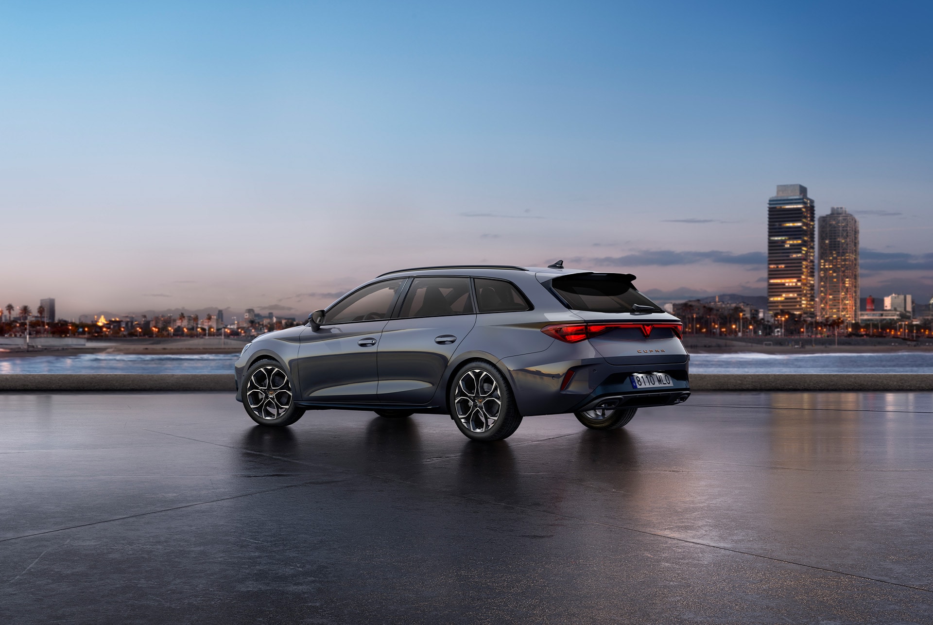 Rear view shot of new Cupra Leon Sportstourer 2025 glossy grey car model with dynamic chassis control, plus black and copper alloy wheels. City in the background at sunset.
