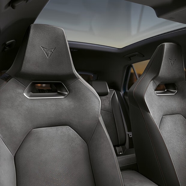 A close-up view of a CUPRA car's interior, showing the headrest and upper section of a CUPRA Bucket seat in dark suede, featuring the embossed CUPRA logo and a panoramic sunroof overhead.