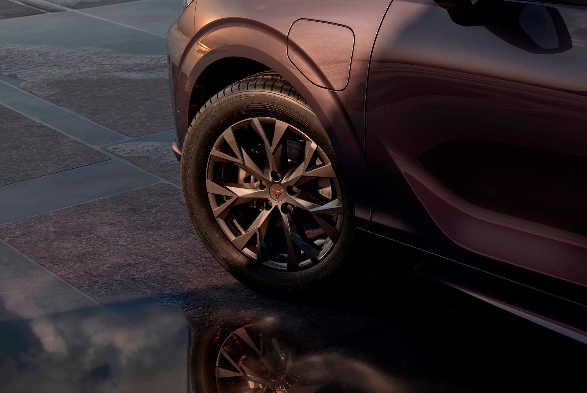 18 inch atomic alloy wheel on the new cupra terramar, in black with copper accents. Background includes a tiled pavement and part of the car's glossy, dark body. 
