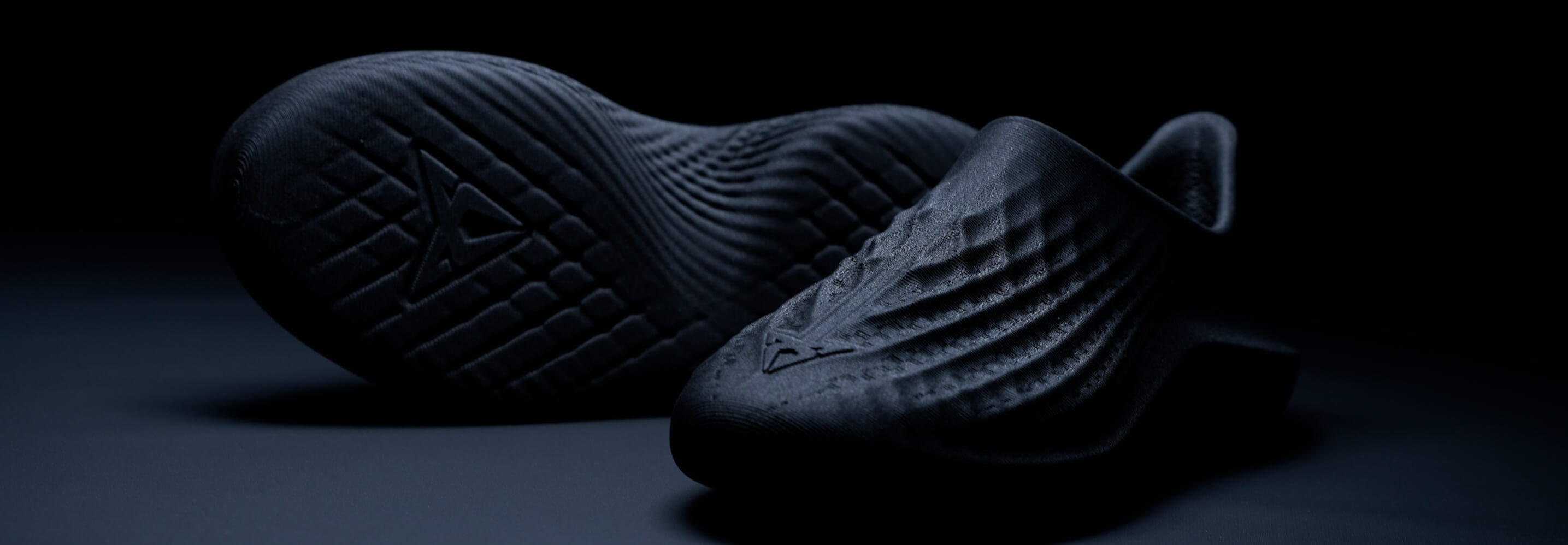 A pair of dark, textured shoes displayed in a product shot against a dark background. A pair of dark, textured shoes displayed in a product shot against a dark background.
