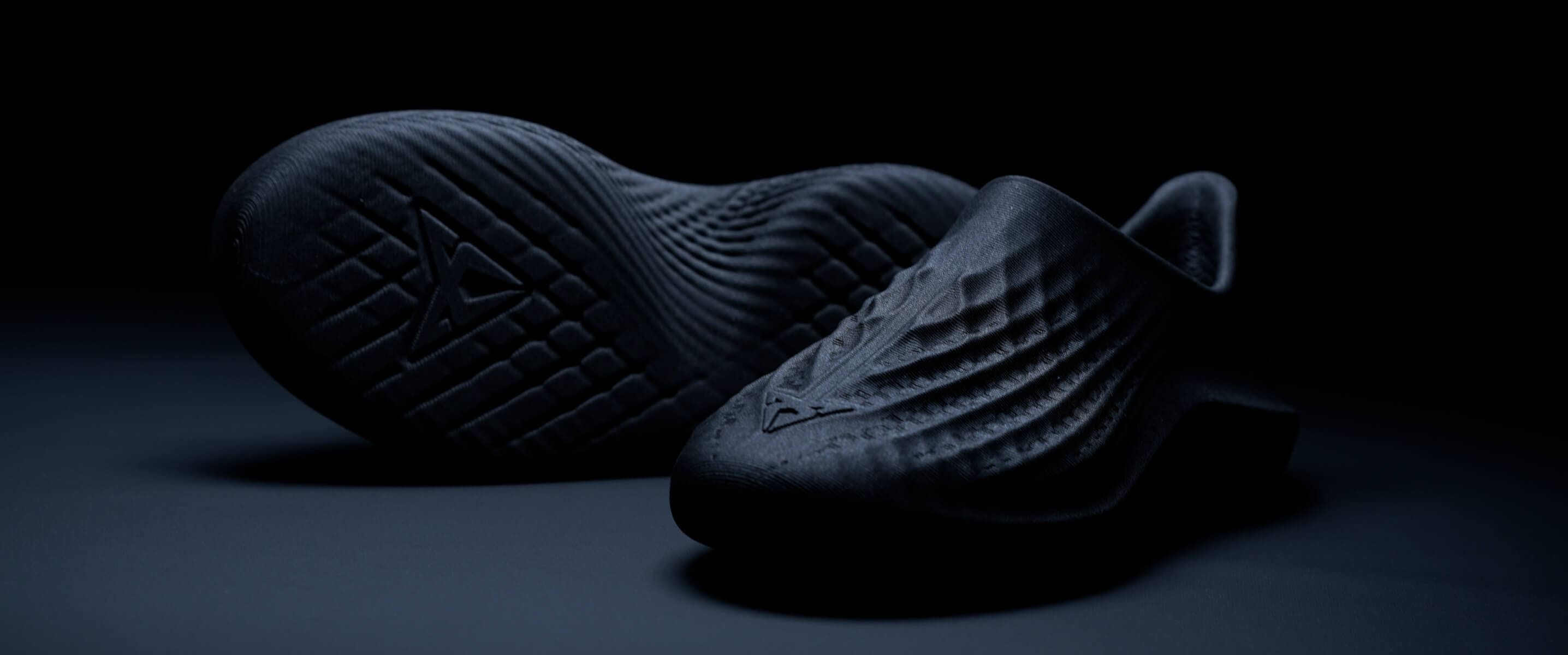 A pair of dark, textured shoes displayed in a product shot against a dark background.