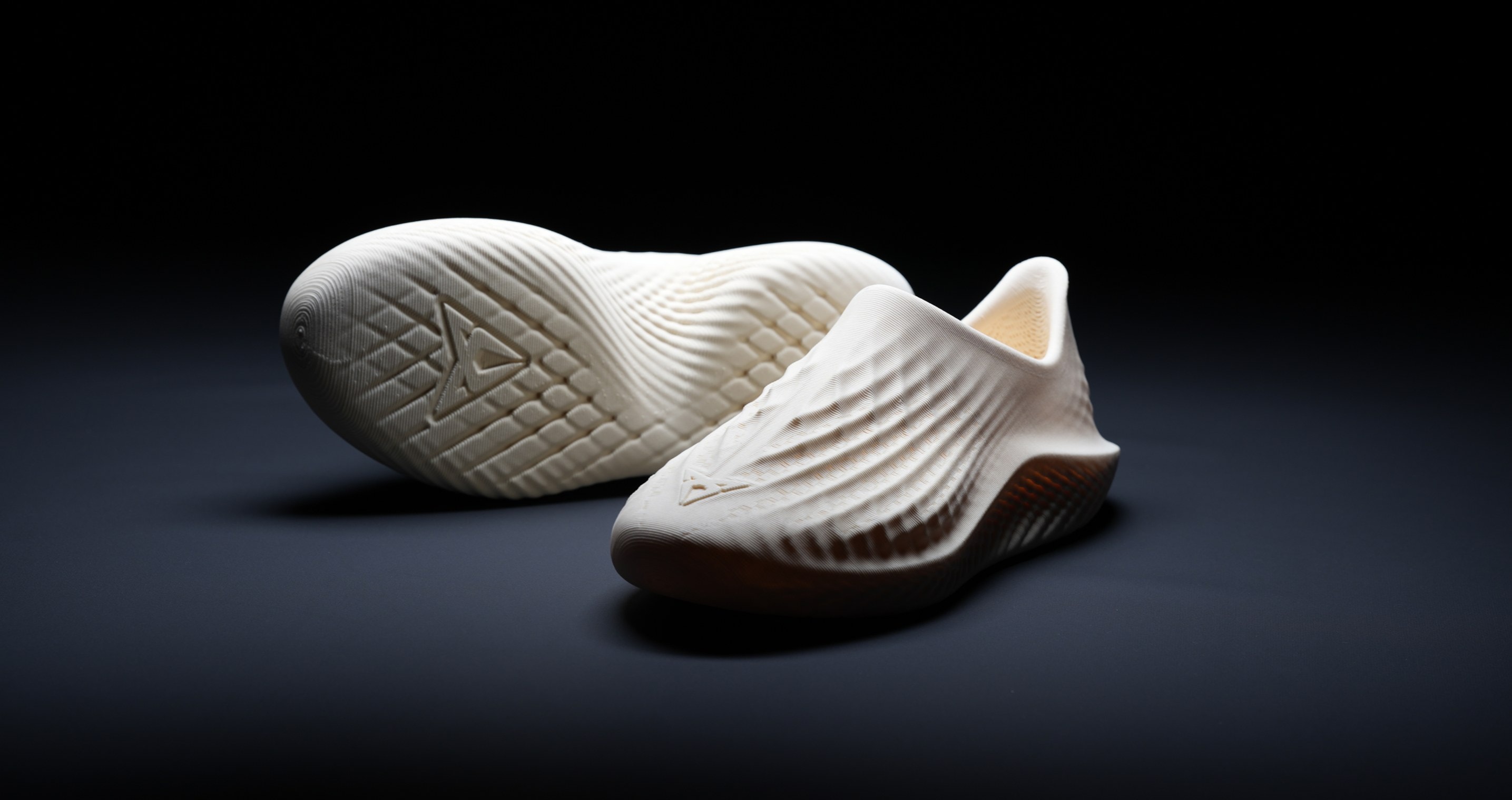 A pair of white, textured shoes displayed in a product shot against a dark background.