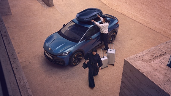 cupra vehicle equipped with a roof boox, designed to add extra storage on your journeys. There are two people next to the car with suitcases.