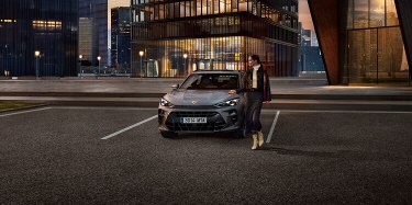 CUPRA Terramar SUV parked in front of sleek modern buildings, with a person standing beside the vehicle.