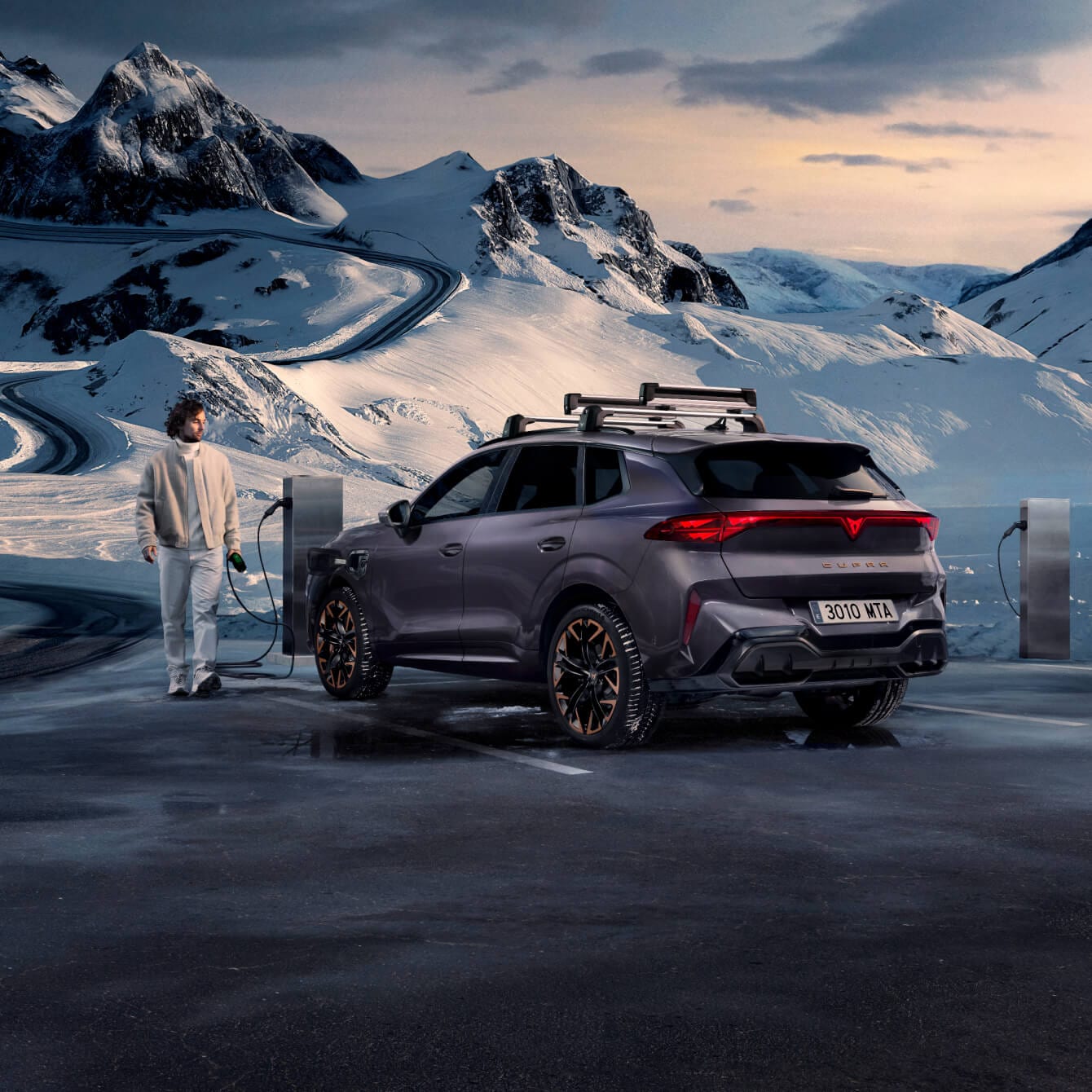 CUPRA Terramar PHEV parked on a snowy mountain road with winding paths and snow-covered peaks in the background.