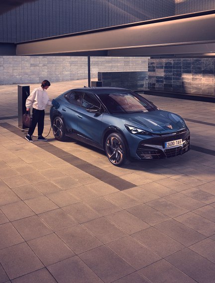 Electric vehicle at charging station, in car park, plugged in by car owner.