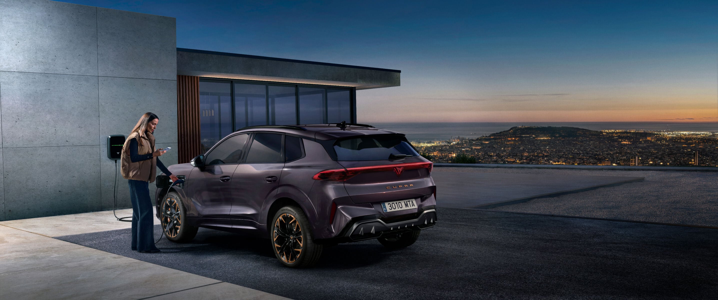  Woman interacting with the My CUPRA App next to a CUPRA Terramar hybrid SUV at a home charging station, highlighting smart connectivity for EV owners.