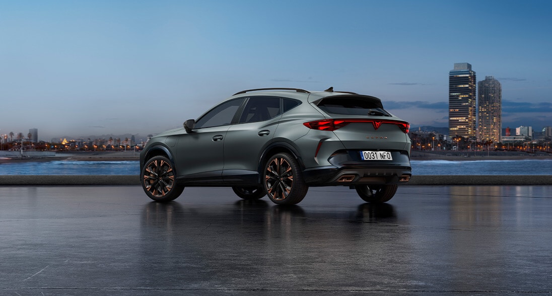 A cupra formentor parked in an outside parking, in the dark with a view of the city in the back.