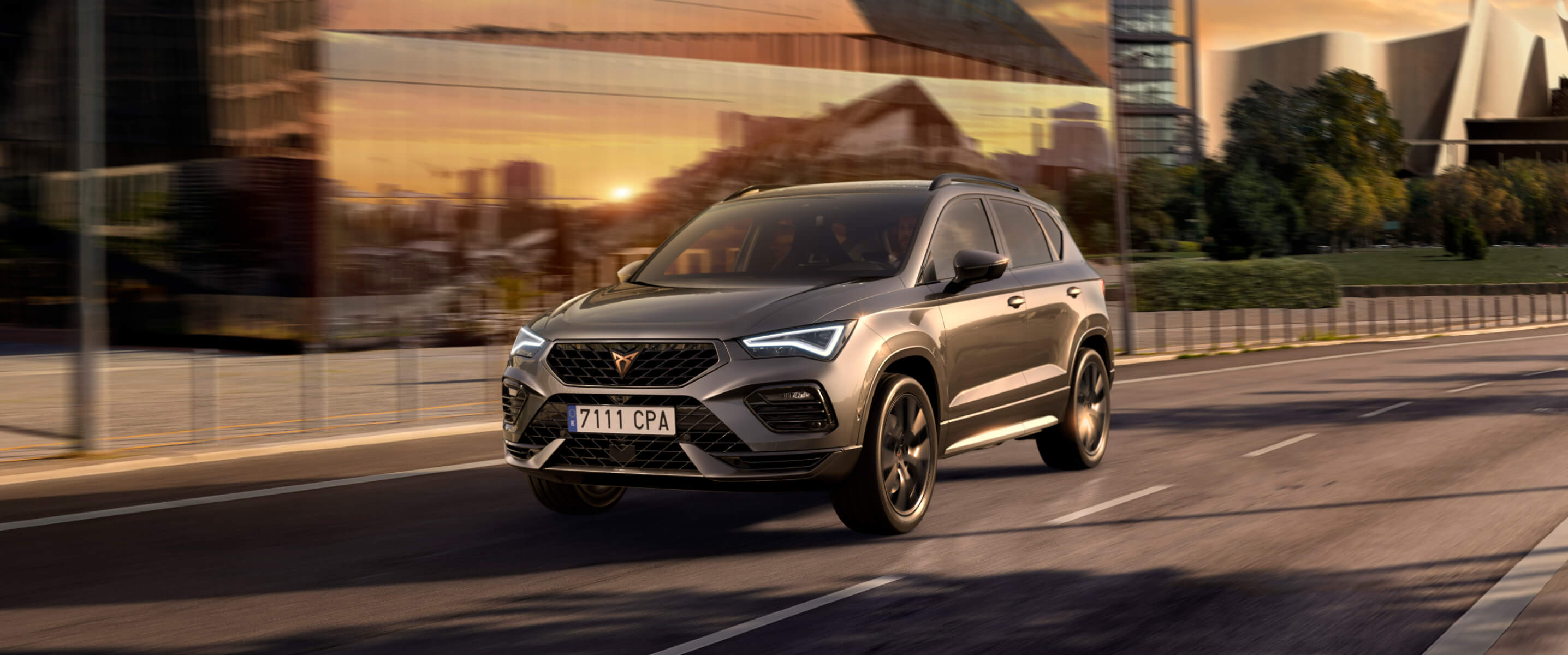 CUPRA Ateca in Graphite Grey, front three-quarter view driving past a modern glass building.