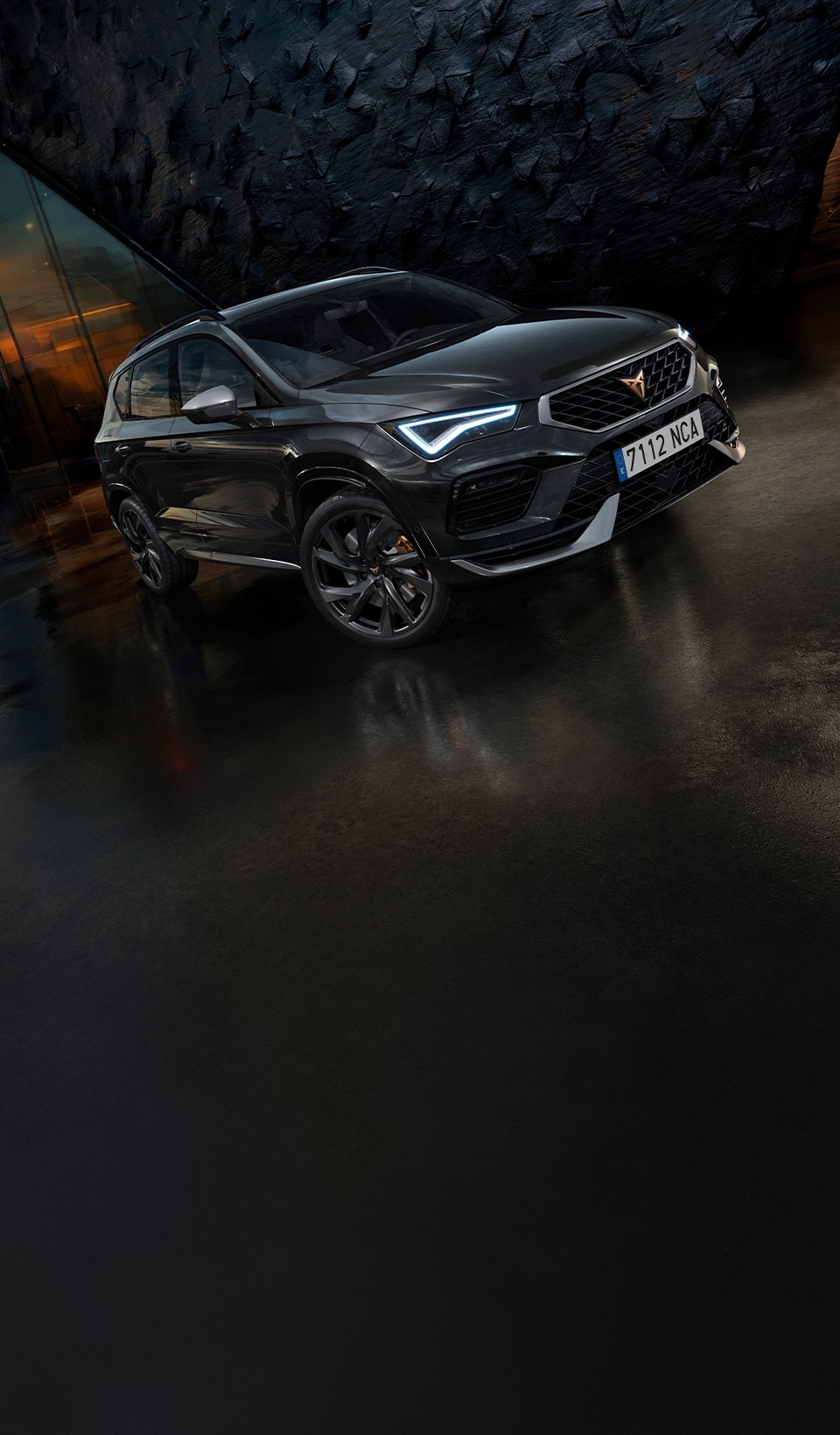 A CUPRA Ateca SUV parked with its front turned slightly towards the viewer, showcasing its distinctive grille, headlights, and copper-accented wheels on blurred background featuring an abstract pattern with a subtly visible human face on the left side.