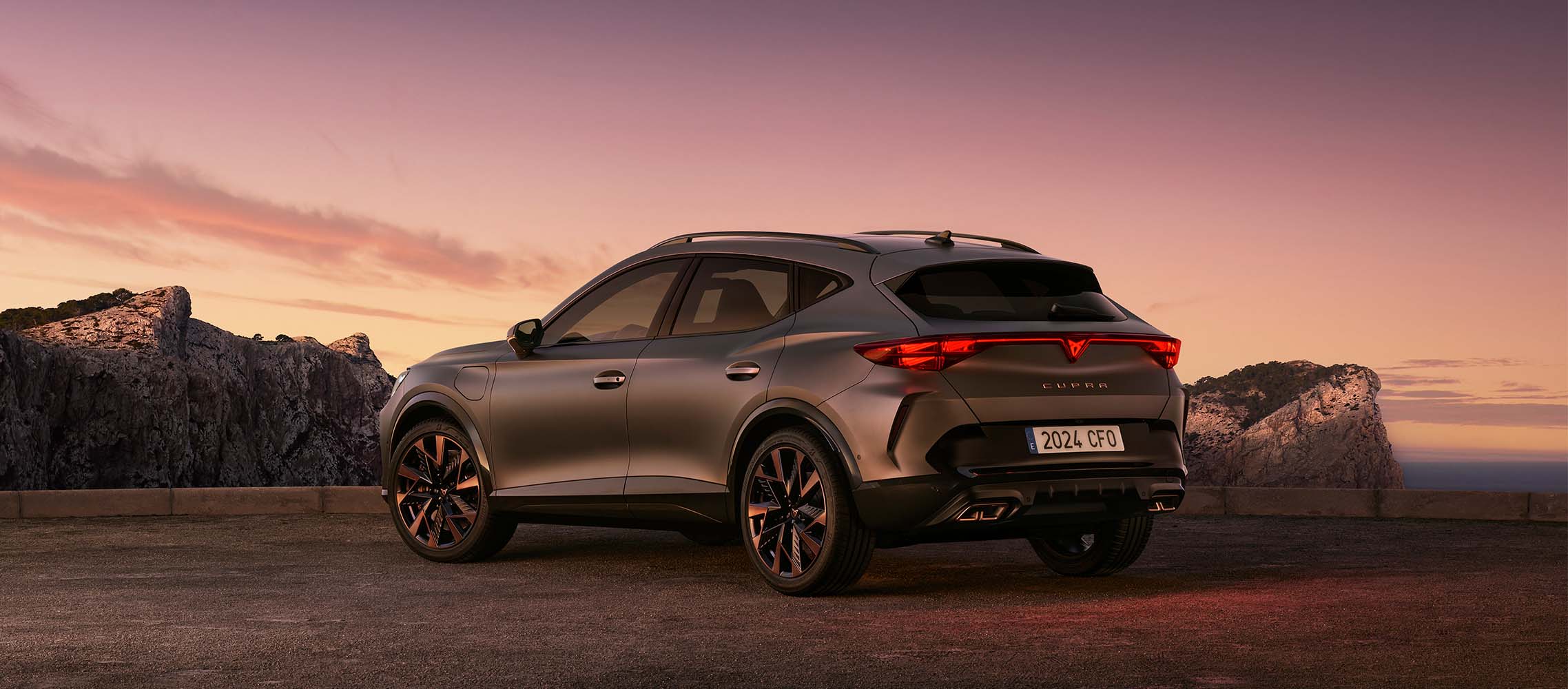 The 2024 CUPRA Formentor parked on a gravel road at sunset, showcasing its sleek metallic grey body and sporty design.